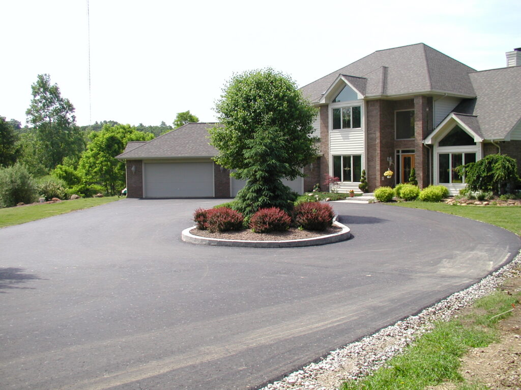 A modern house with a large circular driveway features a central landscaped island with a tree and shrubs, surrounded by lawns and garden beds—all supported by recent foundation repair for lasting stability.