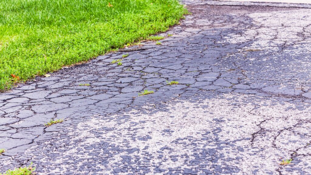 Cracked asphalt pavement next to a patch of green grass, hinting at possible foundation repair needs.