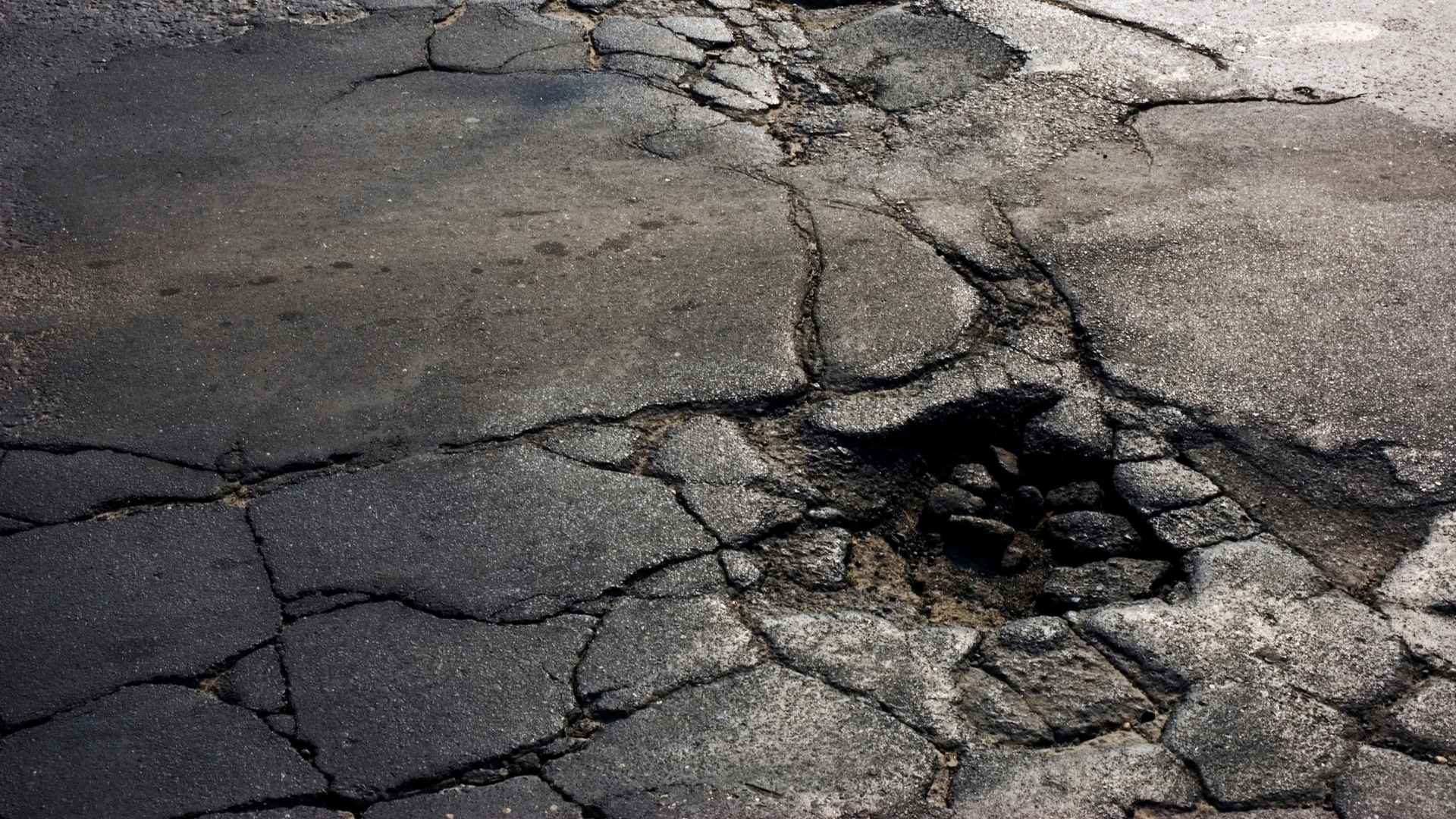 Cracked asphalt road surface with a large pothole