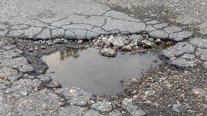 asphalt pothole repair in michigan A pothole filled with water on a cracked, uneven asphalt road.