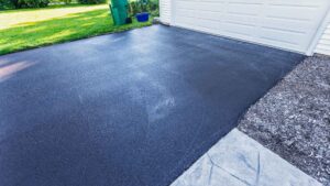 Freshly sealed black asphalt driveway in front of a white garage door