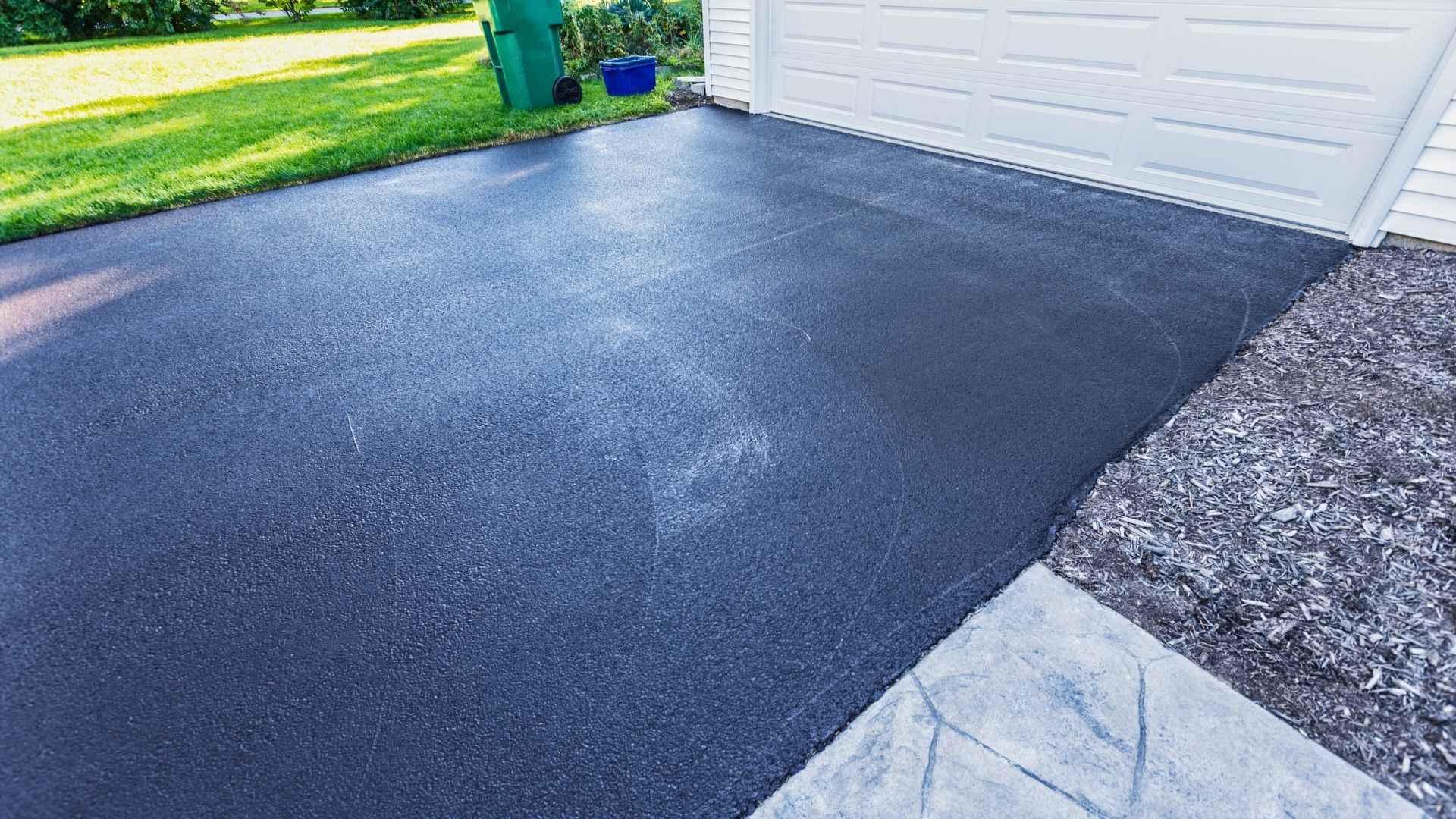 Freshly sealed black asphalt driveway in front of a white garage door