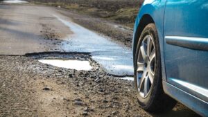 blue car driving towards a paved road with a pothole in the way