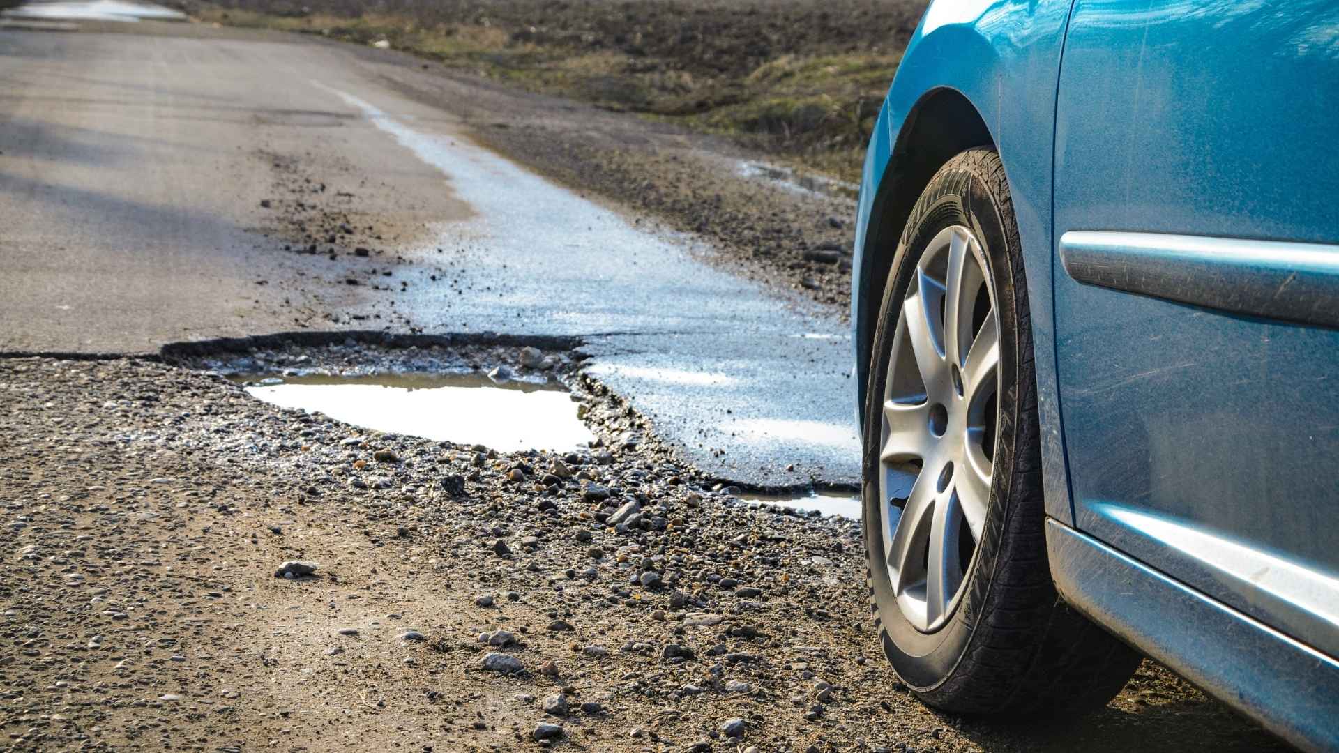 blue car driving towards a paved road with a pothole in the way